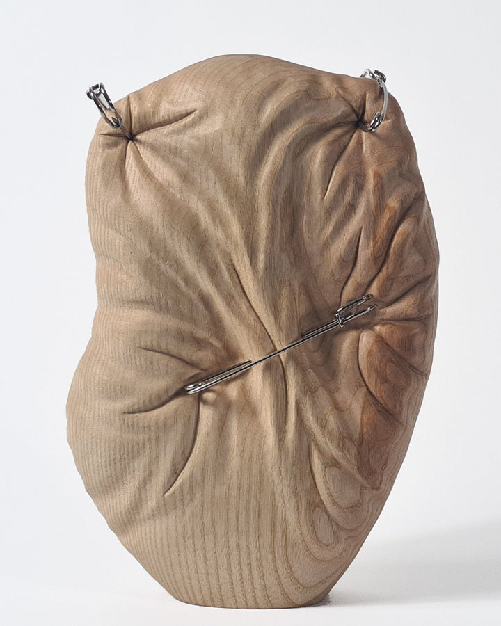 Hand-carved abstract wood sculpture in ash by Bill Prickett, featuring softly contoured organic form pierced with steel pins, creating a visual tension between solid wood and restrained compression.