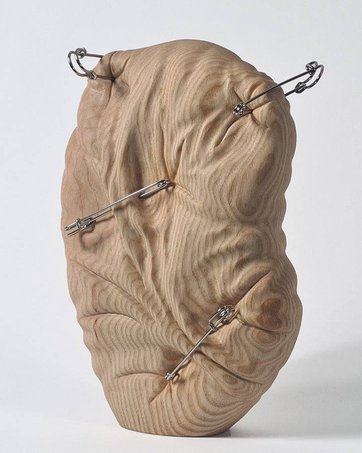 Hand-carved abstract wood sculpture in ash by Bill Prickett, featuring softly contoured organic form pierced with steel pins, creating a visual tension between solid wood and restrained compression.