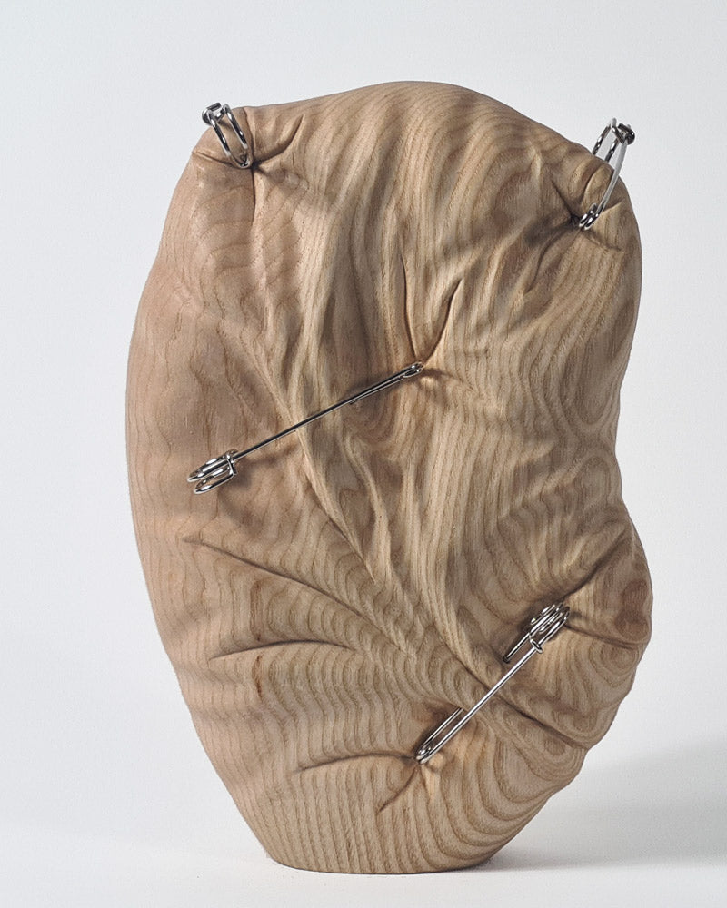 Hand-carved abstract wood sculpture in ash by Bill Prickett, featuring softly contoured organic form pierced with steel pins, creating a visual tension between solid wood and restrained compression.