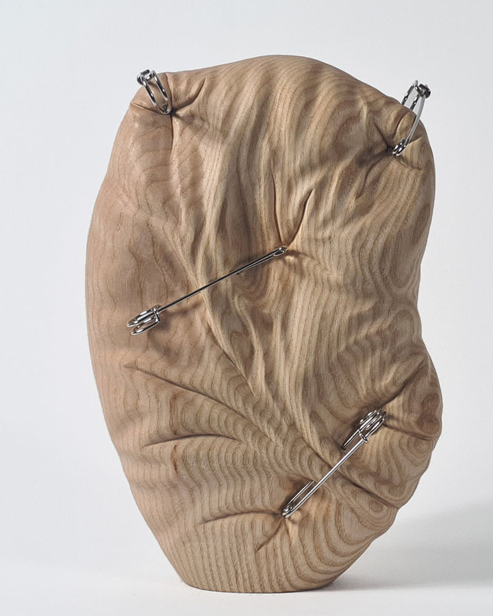 Hand-carved abstract wood sculpture in ash by Bill Prickett, featuring softly contoured organic form pierced with steel pins, creating a visual tension between solid wood and restrained compression.