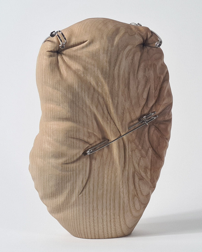 Hand-carved abstract wood sculpture in ash by Bill Prickett, featuring softly contoured organic form pierced with steel pins, creating a visual tension between solid wood and restrained compression.