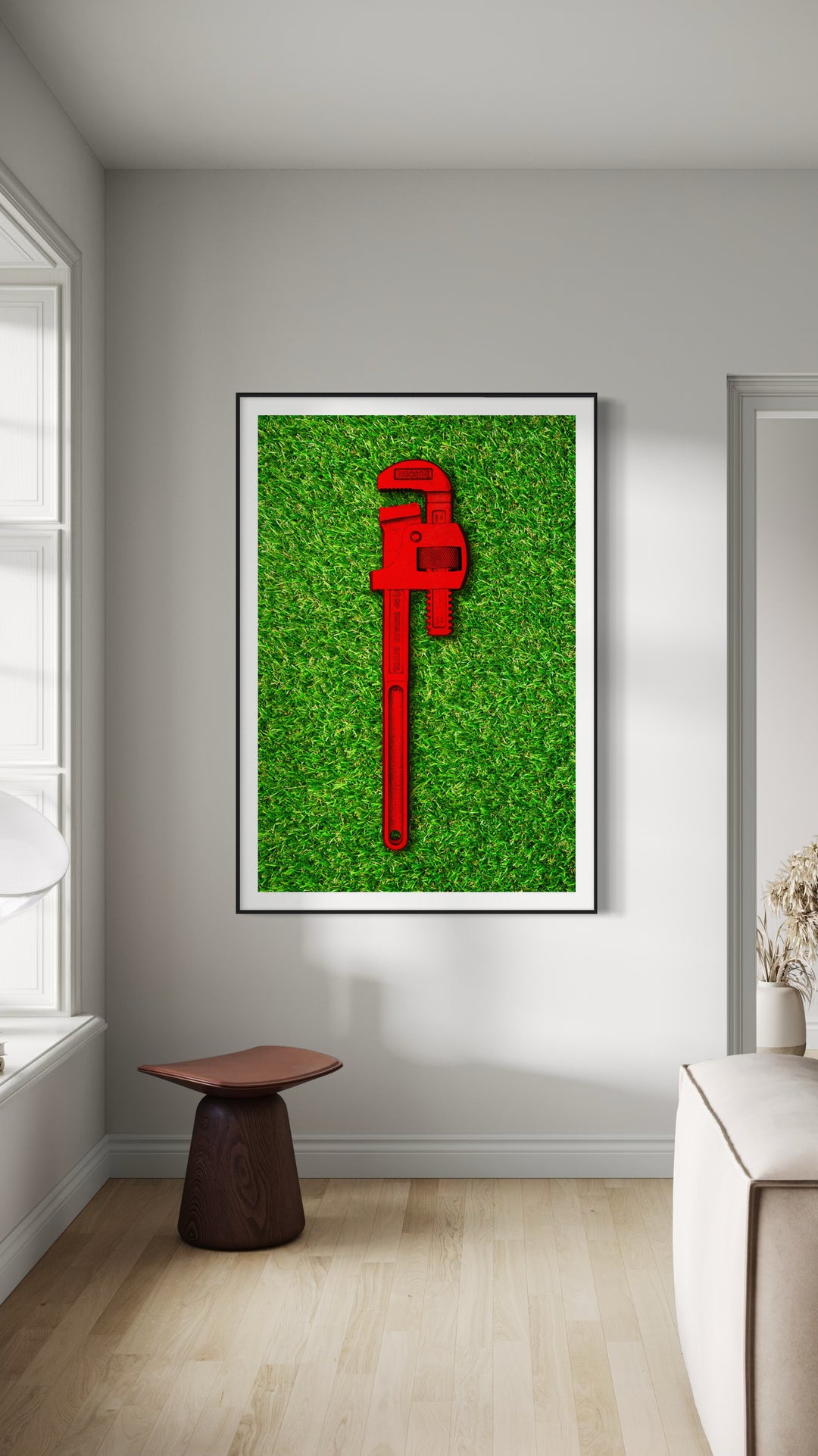 Photograph of a bold red pipe wrench laid flat on vibrant green grass, contrasting industrial form with natural texture.