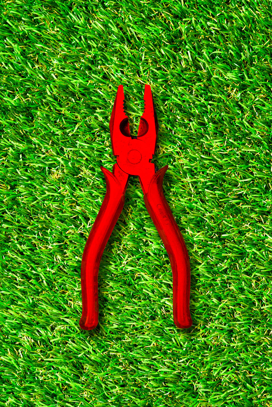 Vibrant photograph of red pliers placed on bright green grass, creating a high-contrast, visually striking composition.