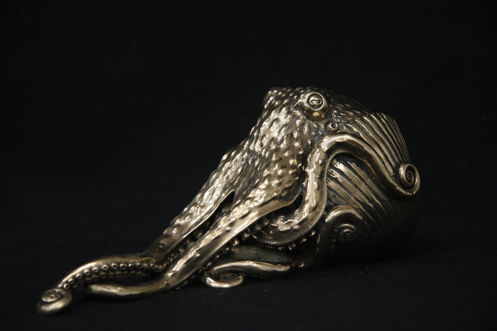 Polished bronze sculpture of an octopus with intricately detailed tentacles and textured body, shown against a black background.