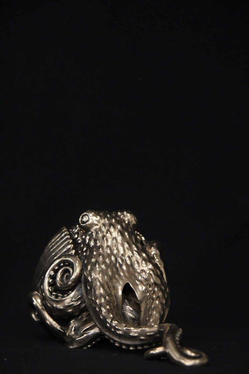 Polished bronze sculpture of an octopus with intricately detailed tentacles and textured body, shown against a black background.