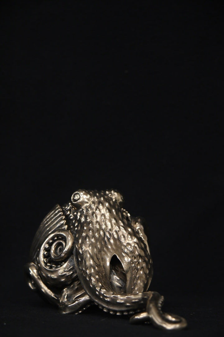 Polished bronze sculpture of an octopus with intricately detailed tentacles and textured body, shown against a black background.