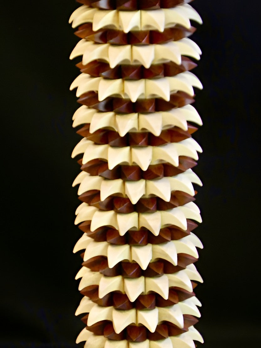 Sculptural table in maple and recycled mahogany, with a cylindrical base of layered pollen-like geometric forms in pale wood and deep red-brown, topped with a smooth circular surface.