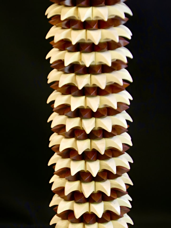 Sculptural table in maple and recycled mahogany, with a cylindrical base of layered pollen-like geometric forms in pale wood and deep red-brown, topped with a smooth circular surface.