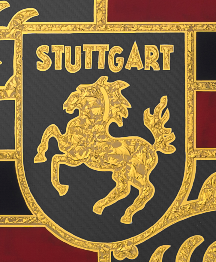 ‘Stuttgart Carbon’ by Vince Edmunds, a handcrafted Porsche automotive artwork featuring the iconic Porsche Stuttgart crest recreated in genuine 24-carat gold leaf and glue-chipped glass. The detailed shield incorporates the prancing Stuttgart horse, ornate gold antlers and lettering, and deep red and black sections against a dark grey carbon fibre background with a visible diagonal weave. Presented in a satin black frame with a fine gold sight line, combining traditional glass gilding with modern motorsport