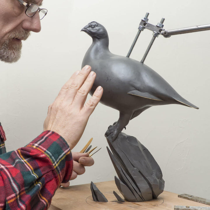 A finely sculpted bronze ptarmigan standing tall on an angular rocky base, with a smooth winter-white patina and soft grey tonality, capturing the bird’s alert posture and clean, rounded form against a neutral backdrop.