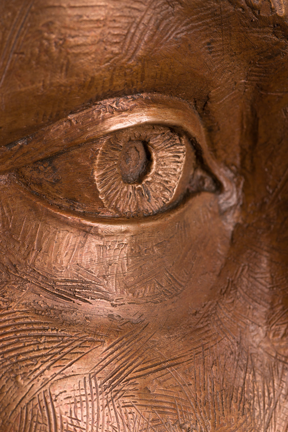Detailed bronze sculpture of a serene female face emerging from a swirling form of honeycomb texture, symbolising a queen bee. The head is crowned with hexagonal cells, flowing seamlessly into a coiled, hive-like base. The surface glows with rich golden and amber tones, celebrating fertility, nature, and the intricate structure of the hive. A bold fusion of natural pattern and human portraiture that highlights the interdependence of bees and humans.