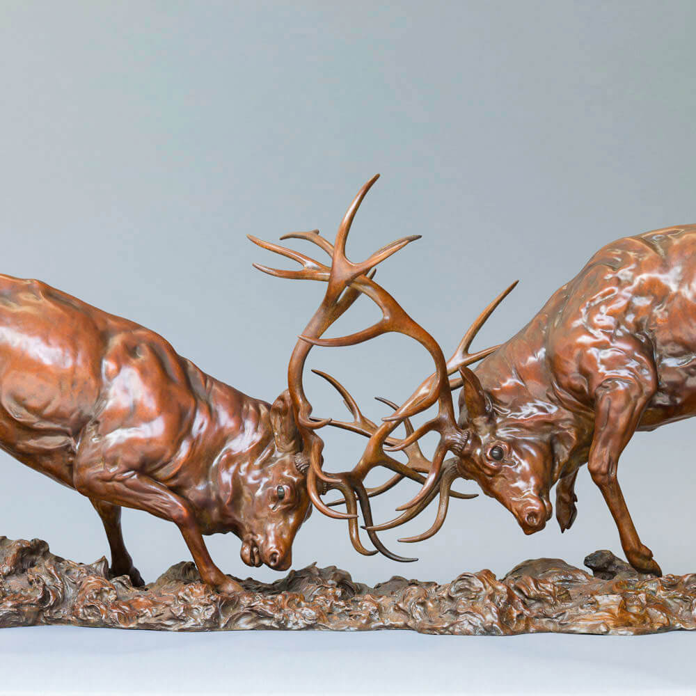 Bronze sculpture of two red deer stags in mid-rut, antlers locked in a dynamic head-to-head clash, highly detailed musculature and patina, mounted on a textured bronze base.