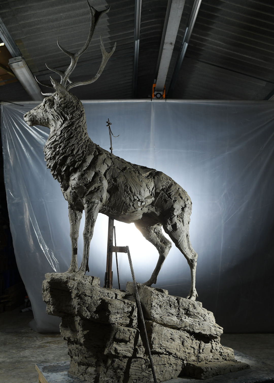 ‘Red Stag: Life Size’ by Hamish Mackie, a monumental limited-edition bronze wildlife sculpture depicting a mature Scottish Highland red deer stag standing alert on a rugged rocky outcrop. Featuring an imposing set of branching antlers, a powerful muscular body and richly textured coat, the sculpture captures the strength, dignity and commanding presence of a stag surveying its territory. Photographs show the original hand-modelled clay sculpture prior to bronze casting.