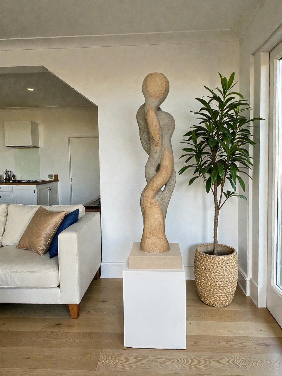 Carved abstract figurative sculpture formed from a single block of Blue and Buff Ancaster Weatherbed stone, with intertwined vertical forms rising from an Ancaster stone plinth, featuring smooth flowing contours, subtle surface texture and balanced proportions designed for indoor display.