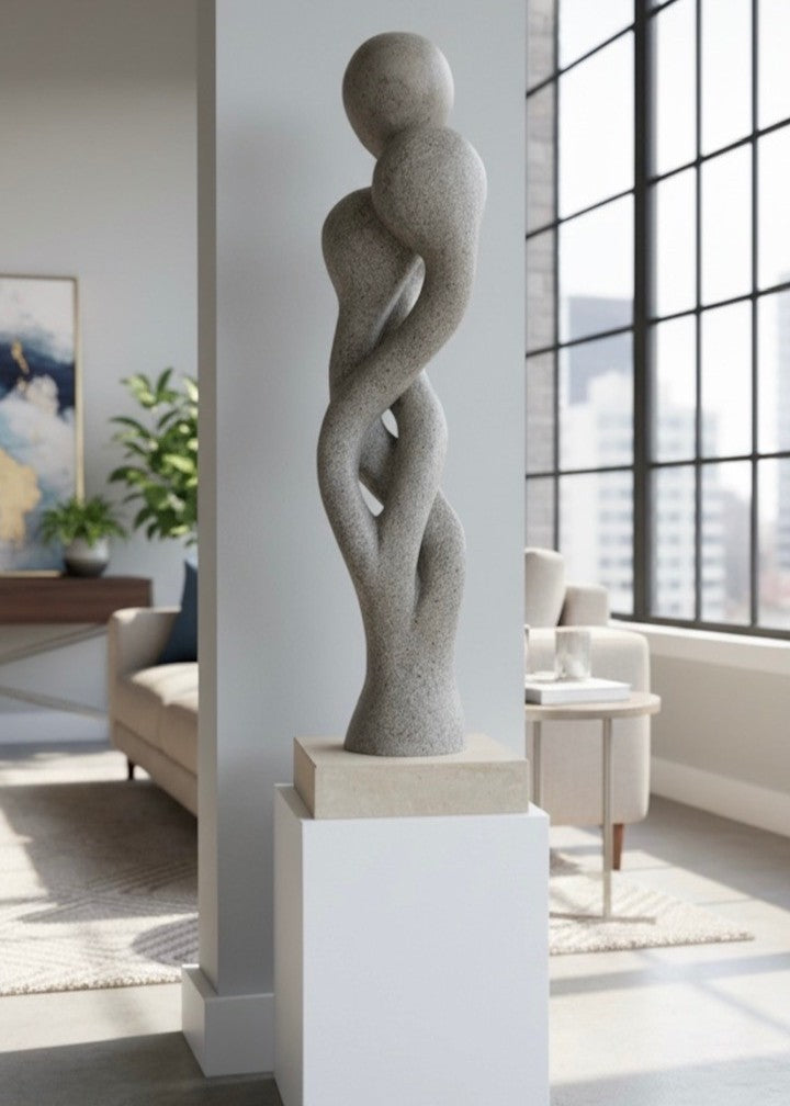 Carved abstract figurative sculpture formed from a single block of Blue and Buff Ancaster Weatherbed stone, with intertwined vertical forms rising from an Ancaster stone plinth, featuring smooth flowing contours, subtle surface texture and balanced proportions designed for indoor display.
