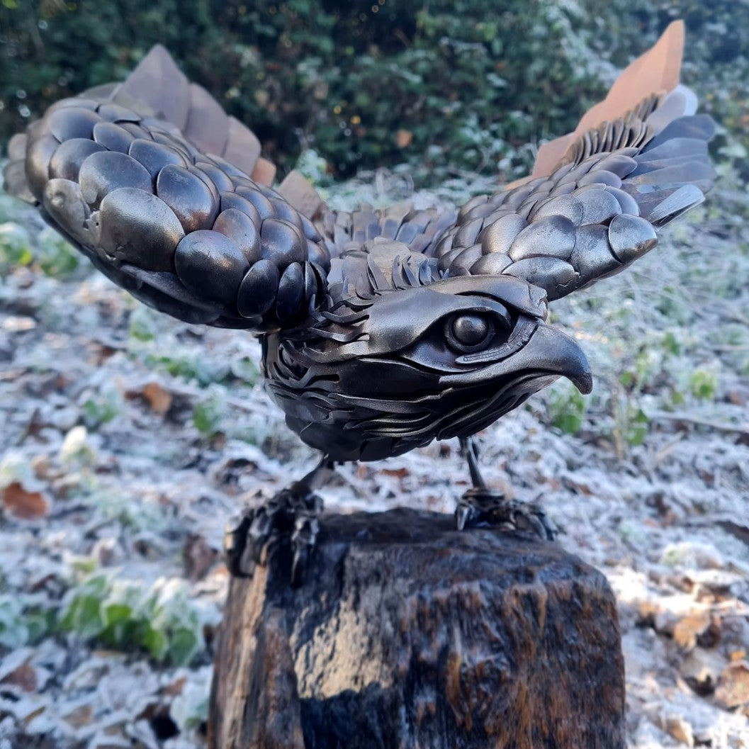 Close-up of a handcrafted metal hawk sculpture with outstretched wings, captured with sparks in the background.