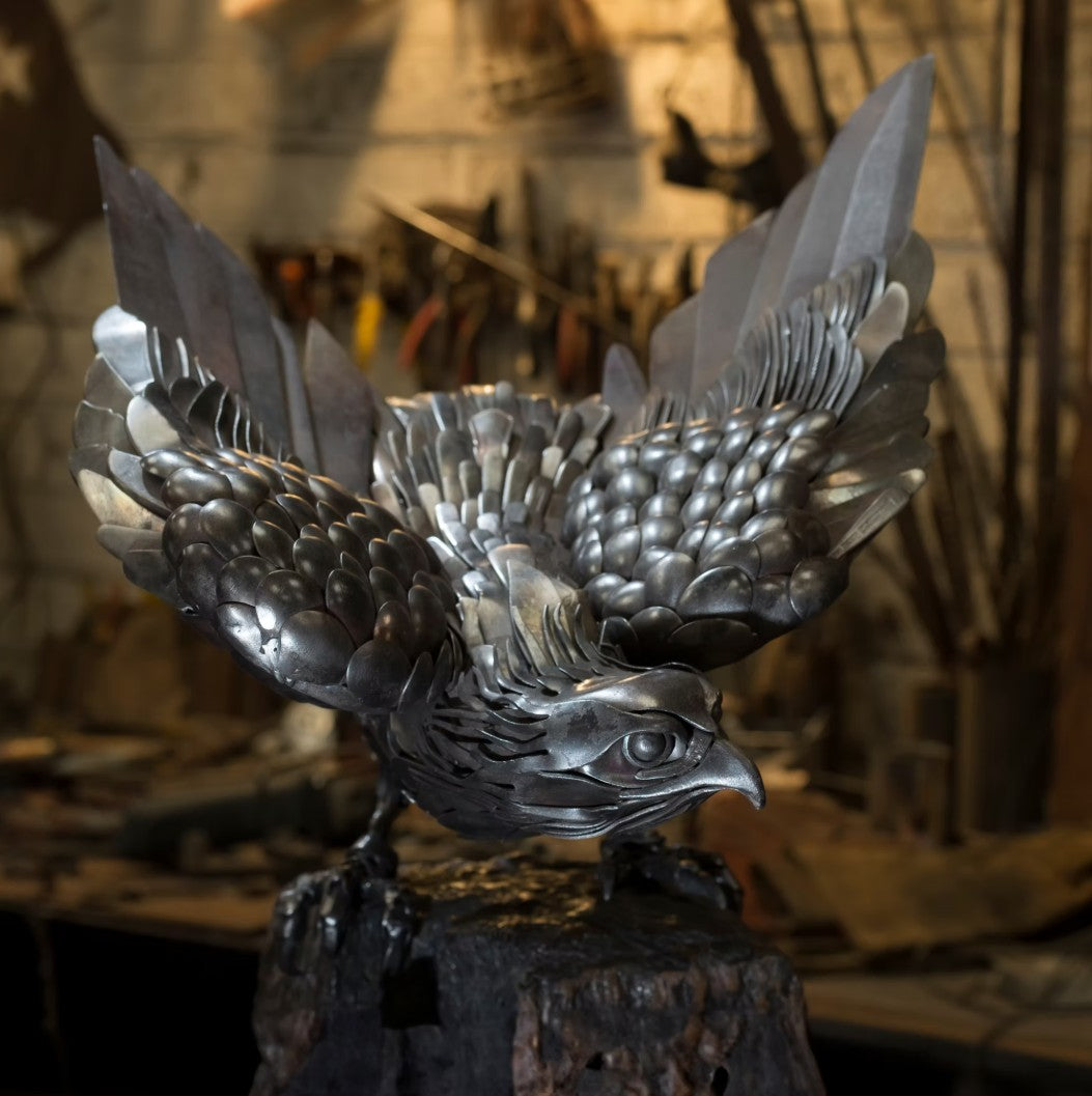 Close-up of a handcrafted metal hawk sculpture with outstretched wings, captured with sparks in the background.