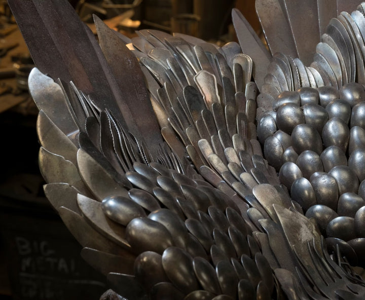 Close-up of a handcrafted metal hawk sculpture with outstretched wings, captured with sparks in the background.