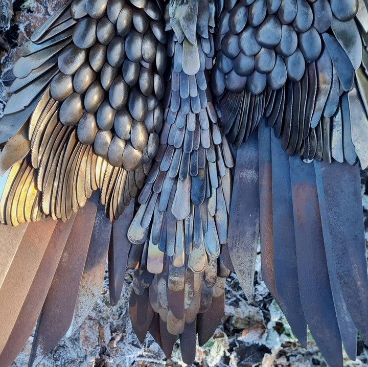 Close-up of a handcrafted metal hawk sculpture with outstretched wings, captured with sparks in the background.