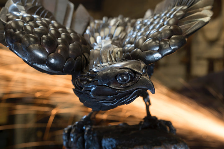 Close-up of a handcrafted metal hawk sculpture with outstretched wings, captured with sparks in the background.