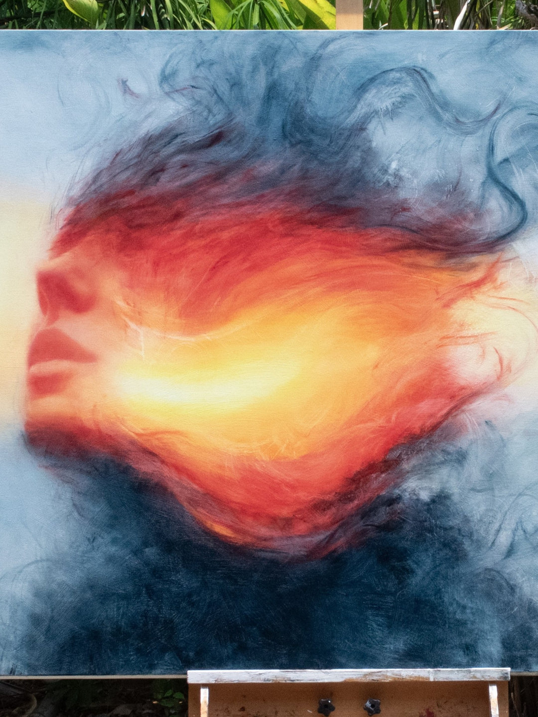 Large oil on canvas painting by Dan Bullock, titled Reverie. A dreamlike portrait of a female face in profile, dissolving into swirling colours of fiery red, orange, and golden yellow, contrasted with cool blue and smoky black tones. The composition radiates energy and motion, blending realism with abstraction.