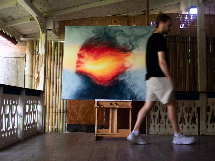 Large oil on canvas painting by Dan Bullock, titled Reverie. A dreamlike portrait of a female face in profile, dissolving into swirling colours of fiery red, orange, and golden yellow, contrasted with cool blue and smoky black tones. The composition radiates energy and motion, blending realism with abstraction.