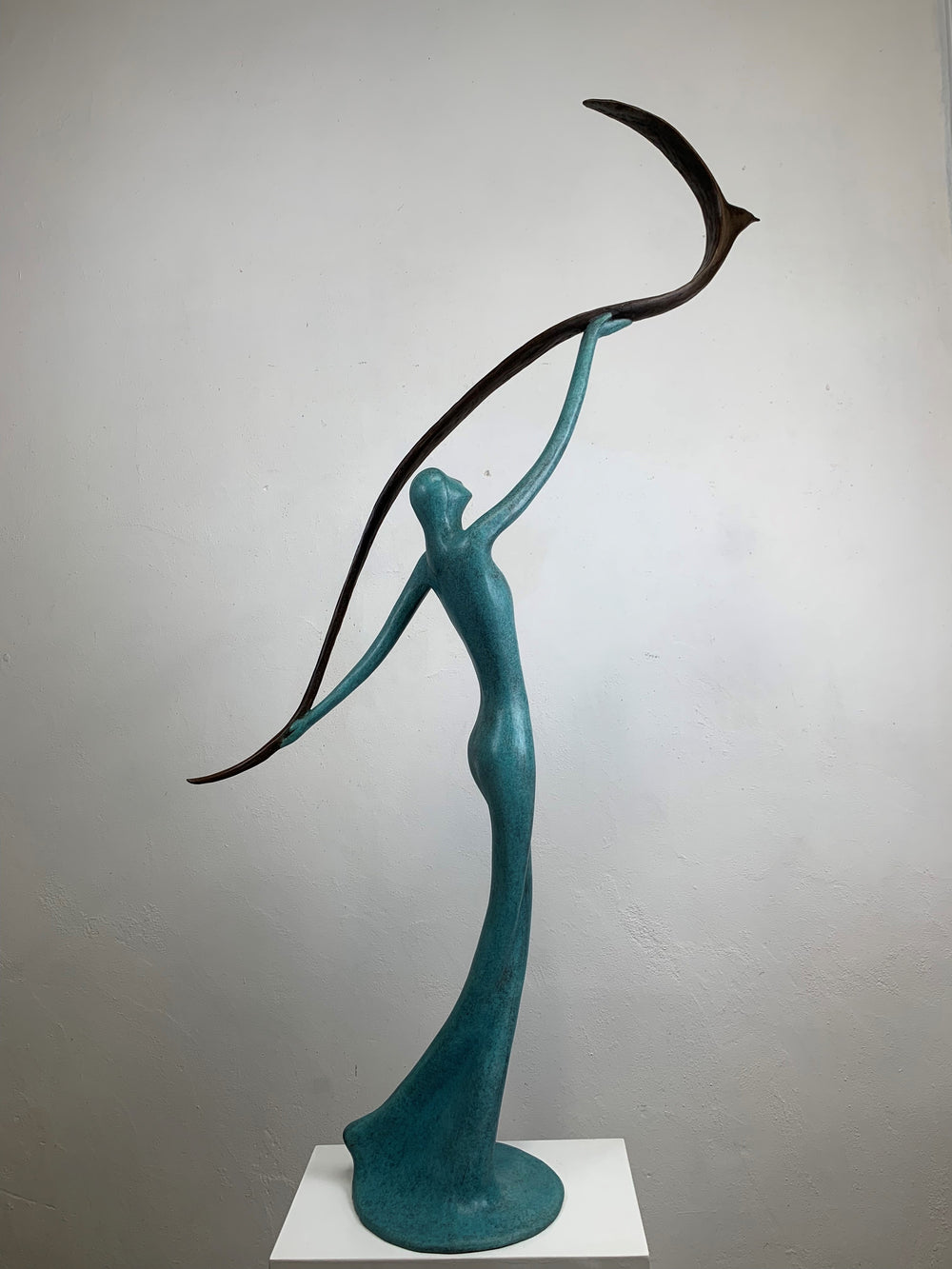 Graceful resin sculpture of an elongated teal figure reaching upward, releasing a stylised bird in flight.