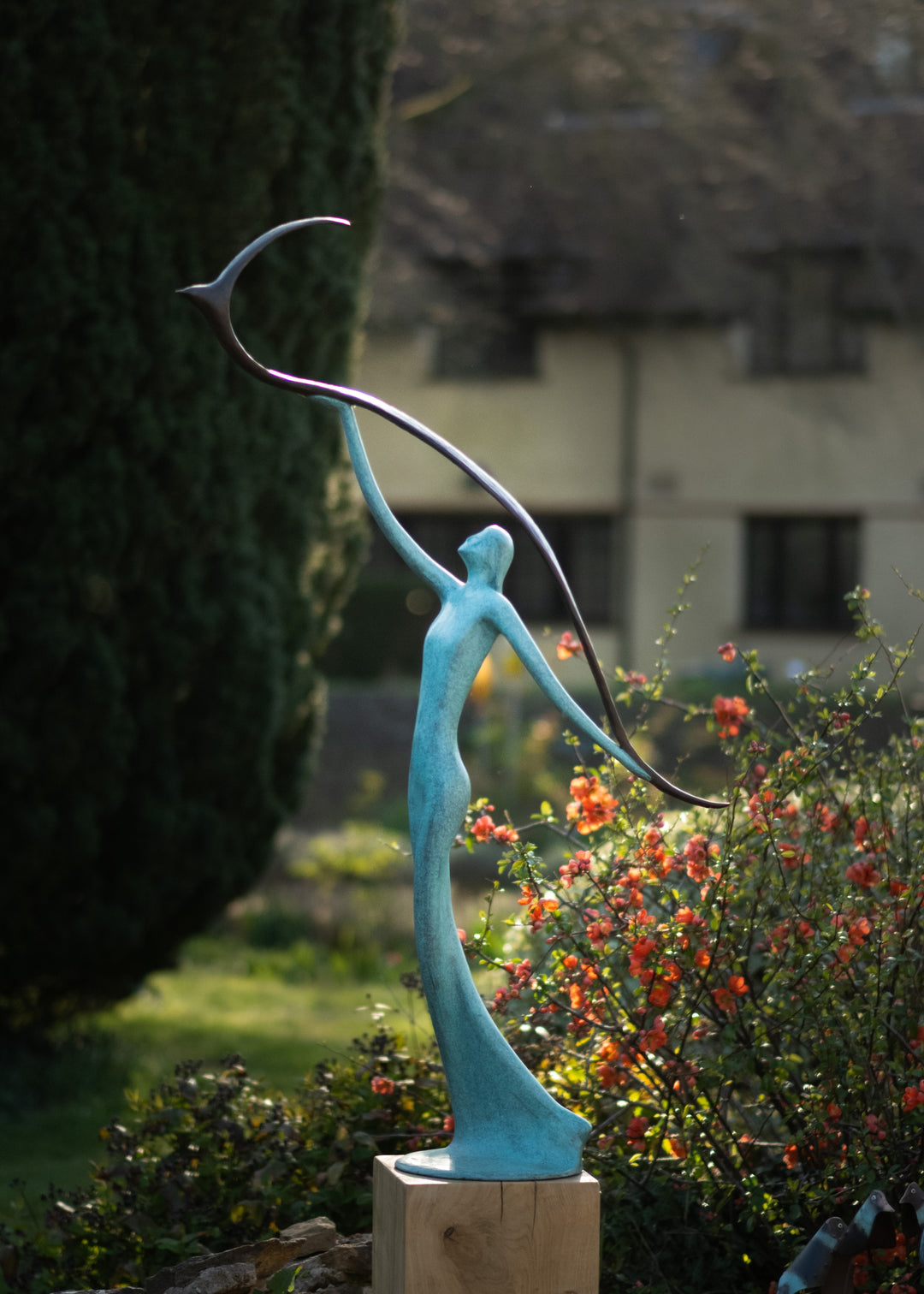Graceful resin sculpture of an elongated teal figure reaching upward, releasing a stylised bird in flight.