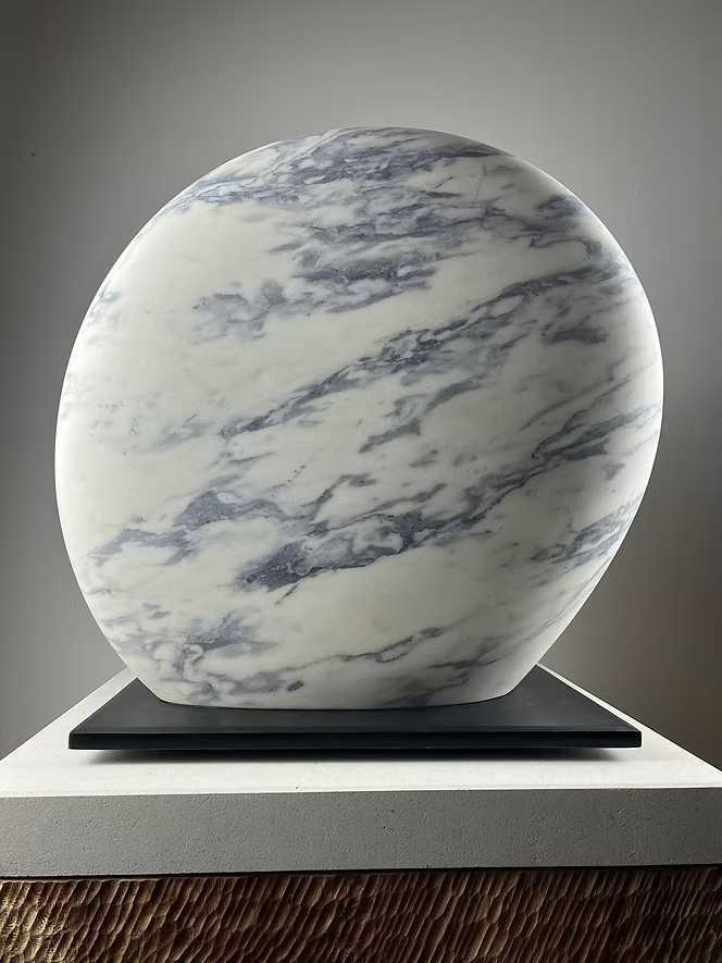 Jason Mulligan sculpture titled RISE, a one-off contemporary abstract artwork hand-carved from Portuguese marble. The sculpture features two large, rounded organic forms rising side by side, their surfaces polished smooth to reveal natural white marble with grey-blue veining. Presented on a black plinth, the piece embodies balance, unity, and quiet strength, blending modern minimalism with timeless stone carving traditions.