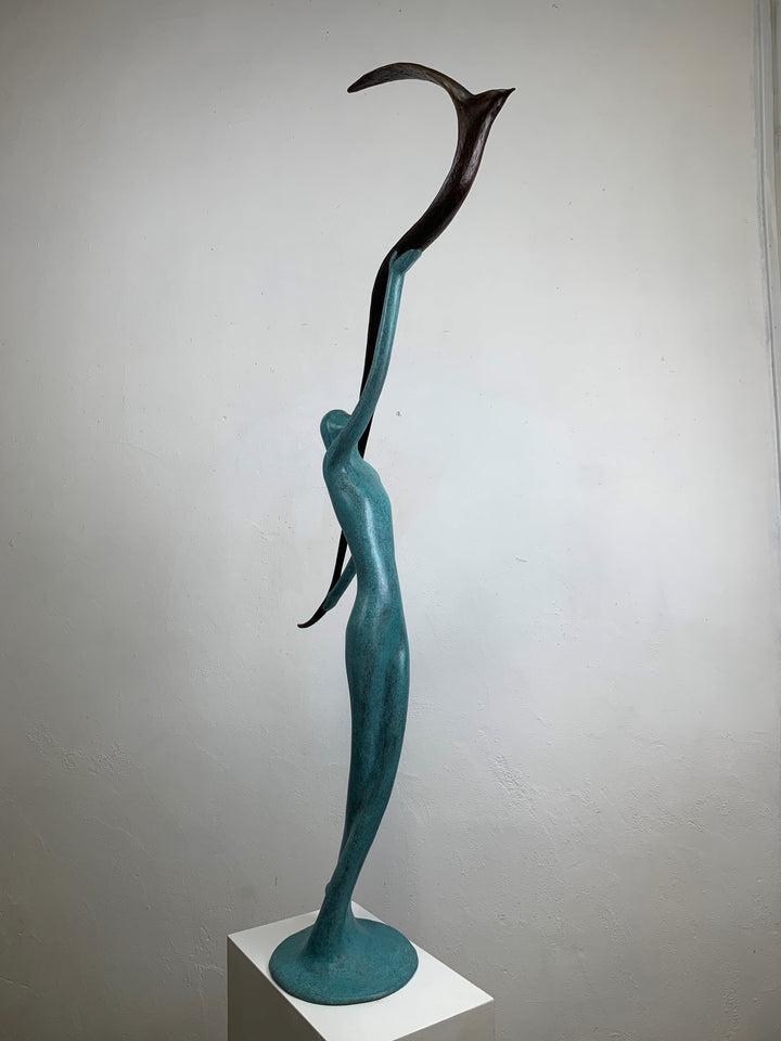 Graceful resin sculpture of an elongated teal figure reaching upward, releasing a stylised bird in flight.