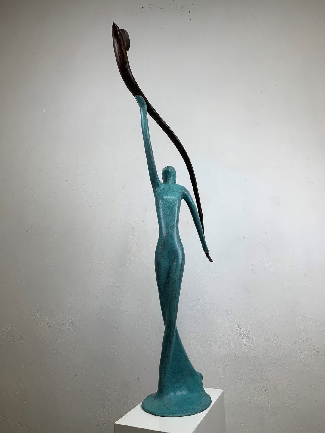 Graceful resin sculpture of an elongated teal figure reaching upward, releasing a stylised bird in flight.