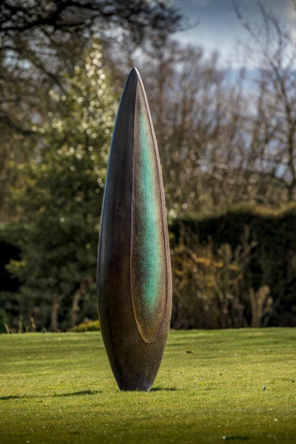 Monumental bronze sculpture by Dominic Welch, Rising Form VI, standing over 2.5 metres tall. The elongated leaf-like form features a smooth, tapering silhouette with a central turquoise-green patinated core against rich bronze tones. A powerful outdoor or architectural piece, it radiates elegance, presence, and organic energy.
