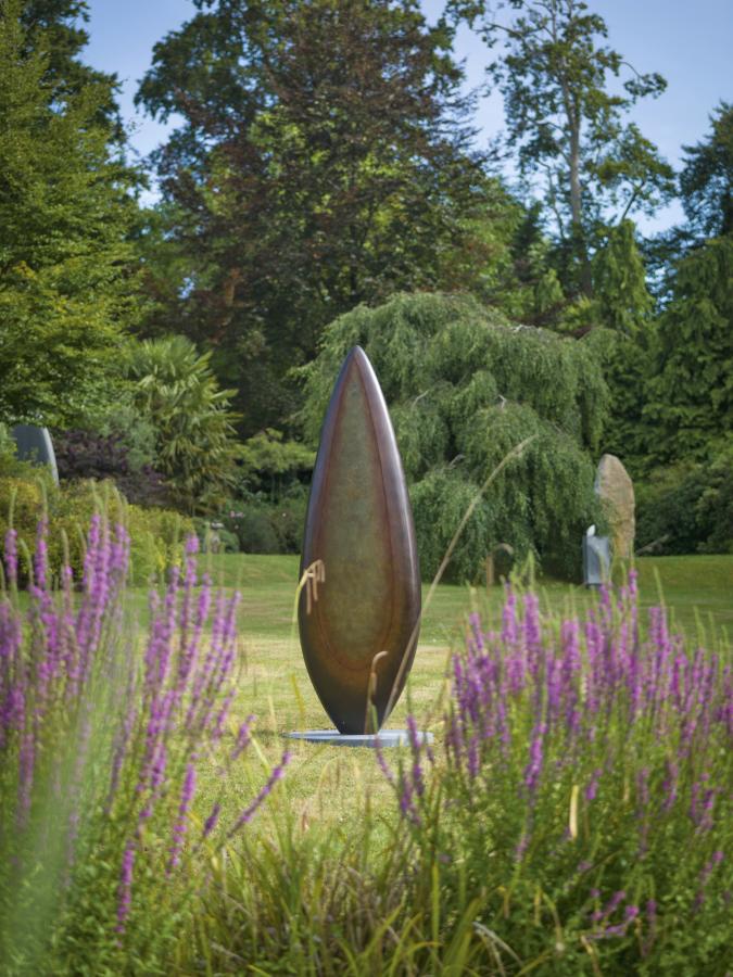 Monumental bronze sculpture by Dominic Welch, Rising Form VI, standing over 2.5 metres tall. The elongated leaf-like form features a smooth, tapering silhouette with a central turquoise-green patinated core against rich bronze tones. A powerful outdoor or architectural piece, it radiates elegance, presence, and organic energy.