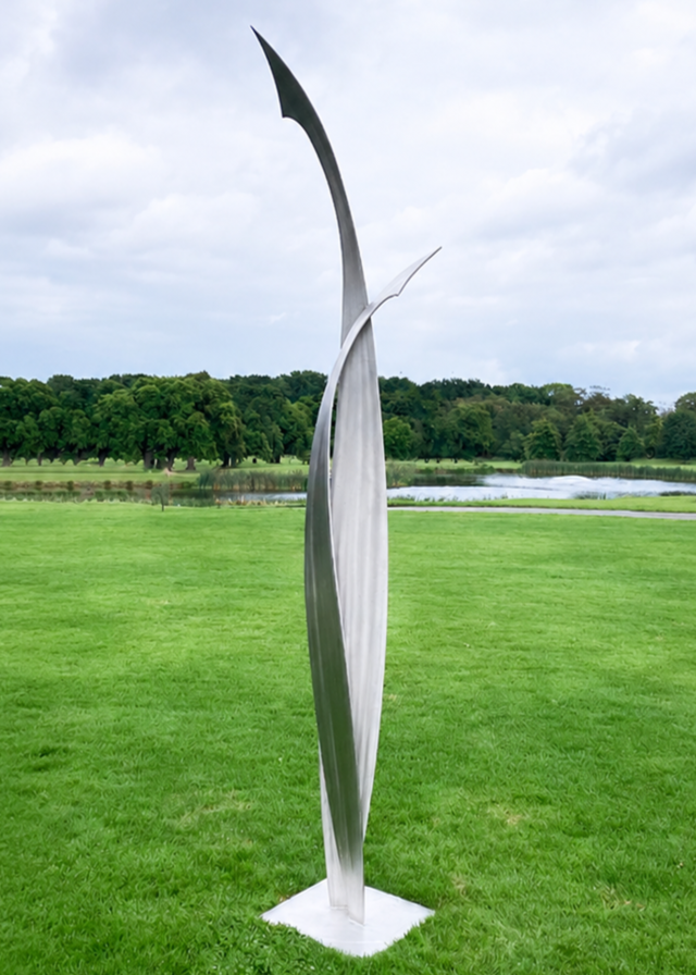 Ian Marlow MRSS stainless steel sculpture Rising Together, featuring two tall, sweeping abstract forms that curve upwards and meet within an elegant contemporary composition, displayed outdoors within a landscaped garden setting.