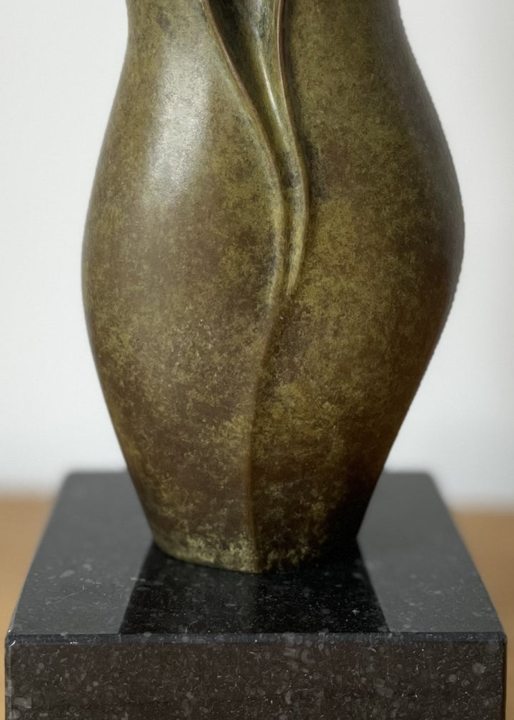 Elegant small bronze sculpture with a fluid, petal-like form and gently folding curves, finished in an earthy green-brown patina with subtle mottling, mounted on a polished black stone base.