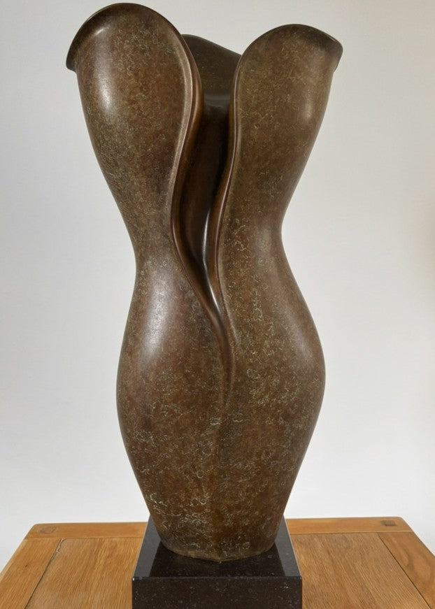 Tall, elegant bronze sculpture with flowing, petal-like curves and a rich earthy brown patina, its organic form rising gracefully from a polished black stone plinth.