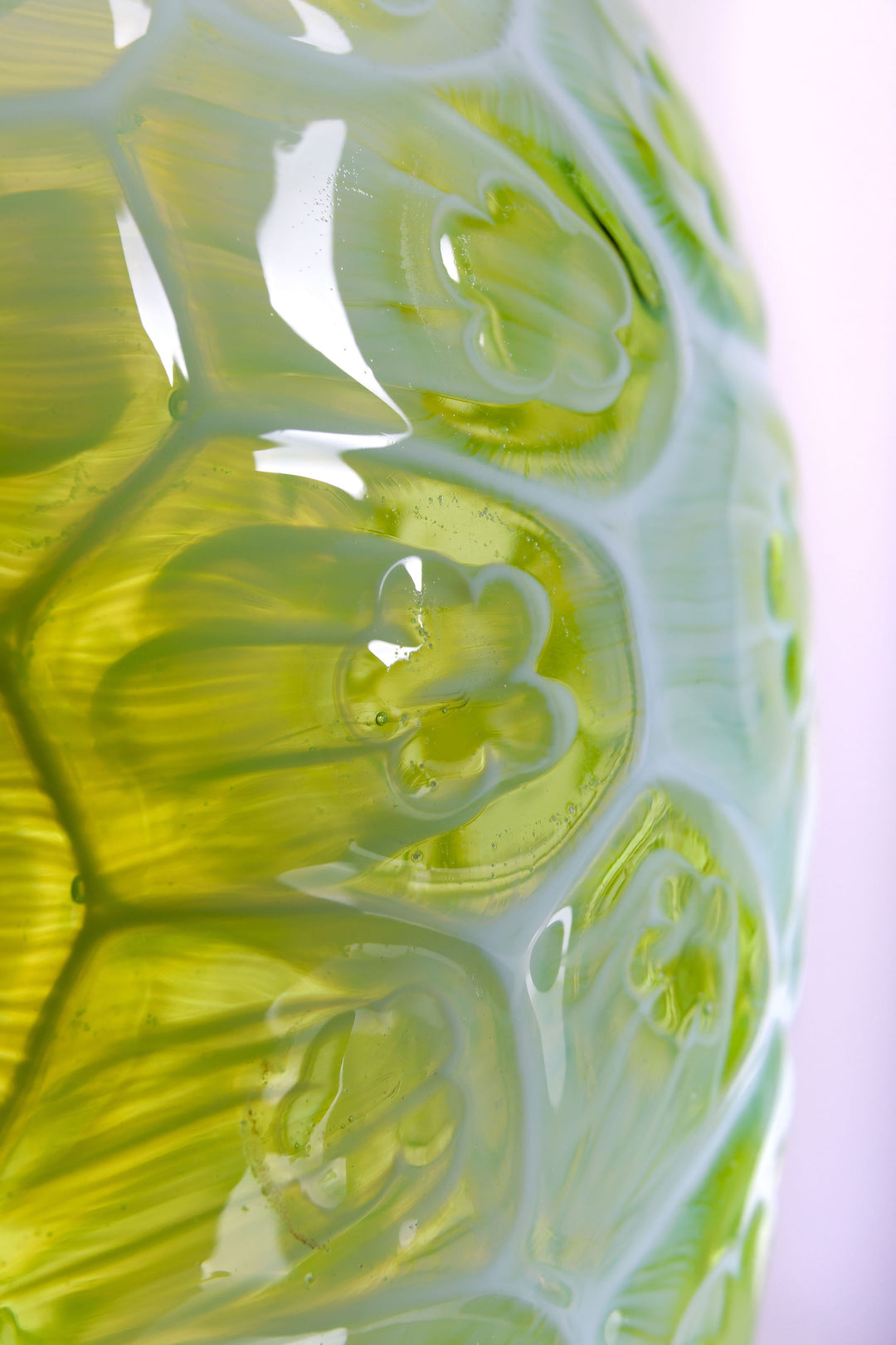 Green hand-blown glass vessel featuring a textured surface with embossed floral motifs and a gently pinched base, shown against a white reflective background.