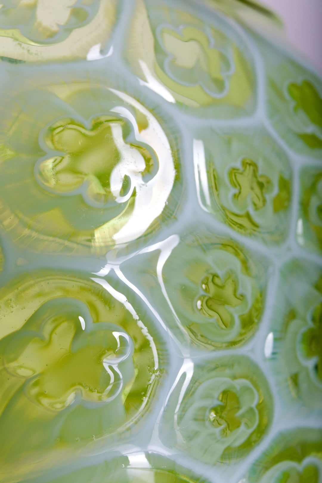 Green hand-blown glass vessel featuring a textured surface with embossed floral motifs and a gently pinched base, shown against a white reflective background.