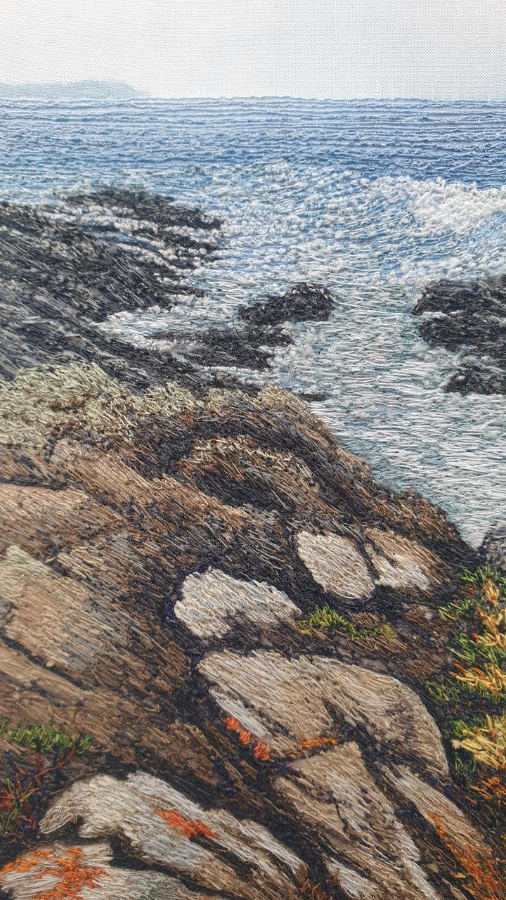 Textile artwork showing coastal rock formations beside the sea, created with freehand machine embroidery on painted silk.