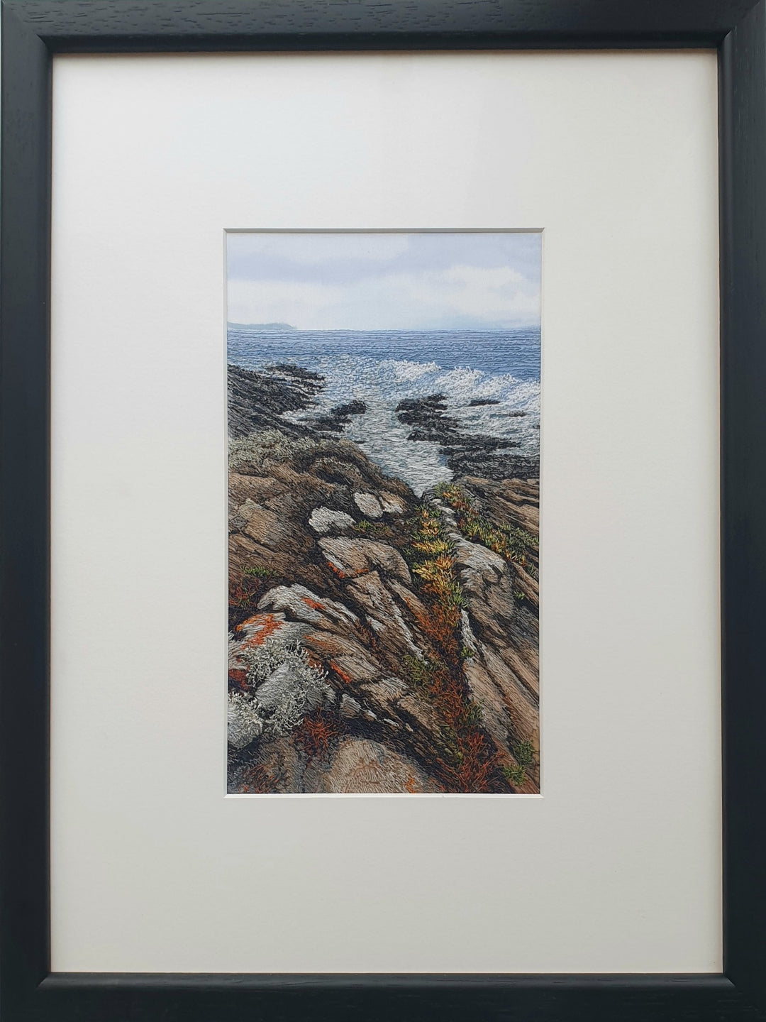 Textile artwork showing coastal rock formations beside the sea, created with freehand machine embroidery on painted silk.