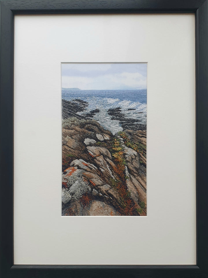 Textile artwork showing coastal rock formations beside the sea, created with freehand machine embroidery on painted silk.