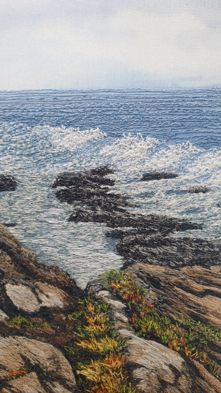Textile artwork showing coastal rock formations beside the sea, created with freehand machine embroidery on painted silk.