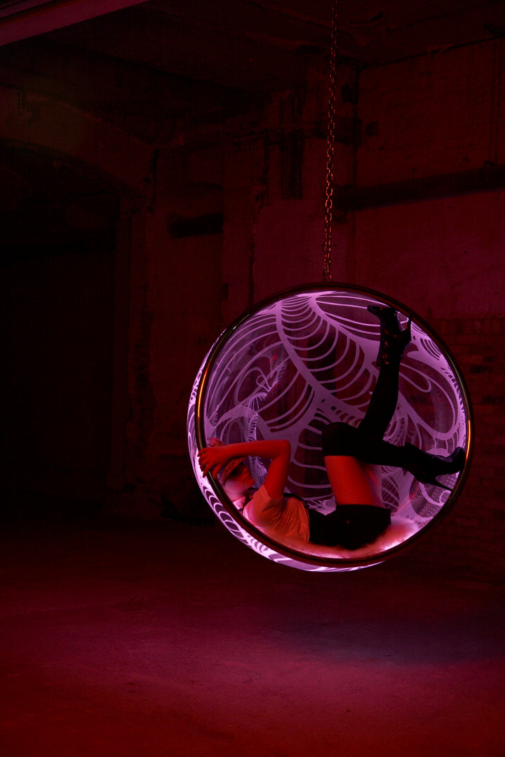 Ben Rousseau, Illuminated Bubble Chair – a limited-edition hanging sphere with engraved acrylic, vibrant pink-purple LED glow, and Mongolian sheepskin cushion featuring INSA’s signature pattern. A cocoon-like statement chair blending art, comfort, and sensory light.