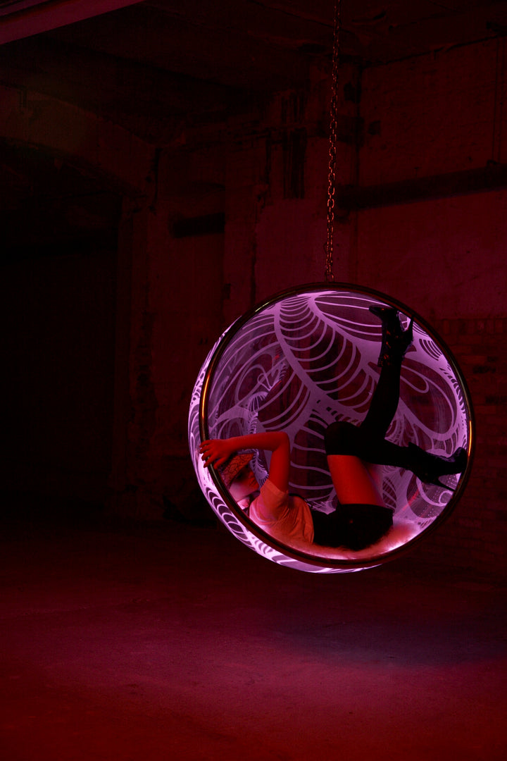 Ben Rousseau, Illuminated Bubble Chair – a limited-edition hanging sphere with engraved acrylic, vibrant pink-purple LED glow, and Mongolian sheepskin cushion featuring INSA’s signature pattern. A cocoon-like statement chair blending art, comfort, and sensory light.