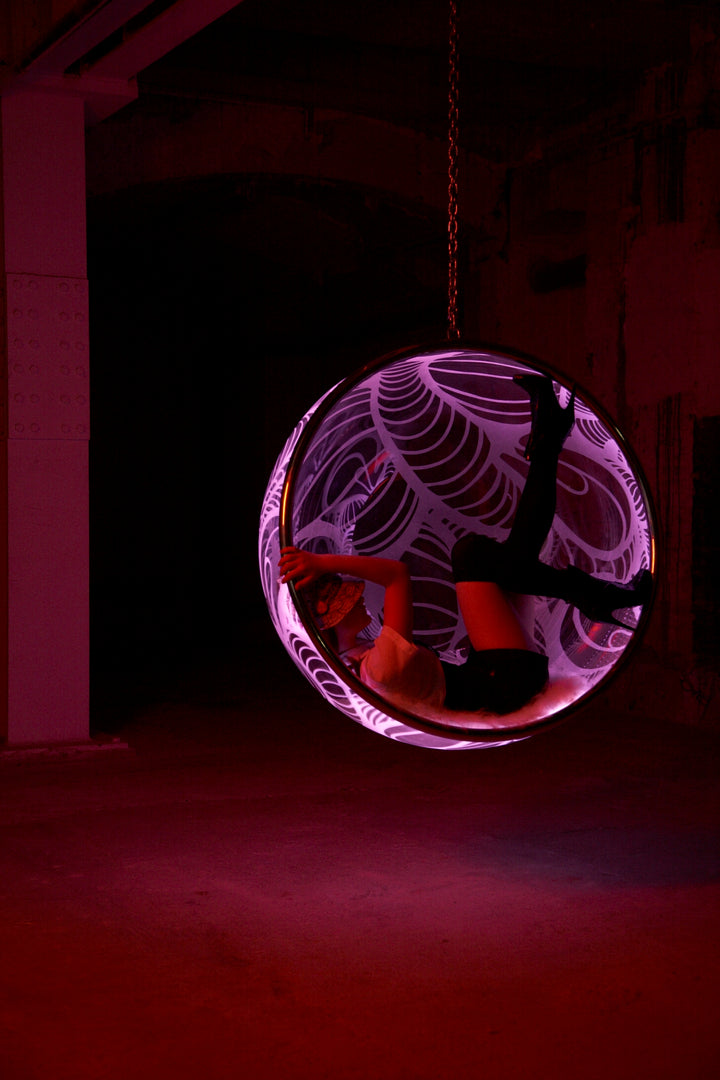 Ben Rousseau, Illuminated Bubble Chair – a limited-edition hanging sphere with engraved acrylic, vibrant pink-purple LED glow, and Mongolian sheepskin cushion featuring INSA’s signature pattern. A cocoon-like statement chair blending art, comfort, and sensory light.