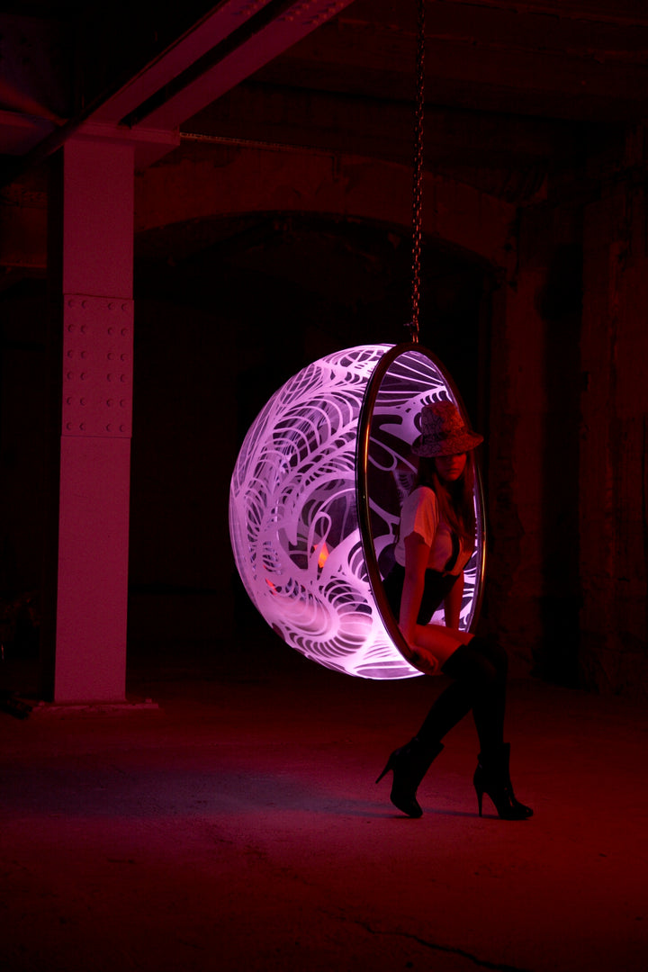 Ben Rousseau, Illuminated Bubble Chair – a limited-edition hanging sphere with engraved acrylic, vibrant pink-purple LED glow, and Mongolian sheepskin cushion featuring INSA’s signature pattern. A cocoon-like statement chair blending art, comfort, and sensory light.