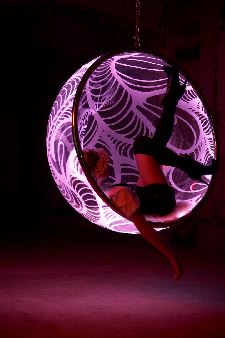 Ben Rousseau, Illuminated Bubble Chair – a limited-edition hanging sphere with engraved acrylic, vibrant pink-purple LED glow, and Mongolian sheepskin cushion featuring INSA’s signature pattern. A cocoon-like statement chair blending art, comfort, and sensory light.