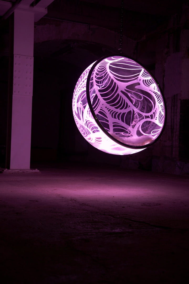 Ben Rousseau, Illuminated Bubble Chair – a limited-edition hanging sphere with engraved acrylic, vibrant pink-purple LED glow, and Mongolian sheepskin cushion featuring INSA’s signature pattern. A cocoon-like statement chair blending art, comfort, and sensory light.
