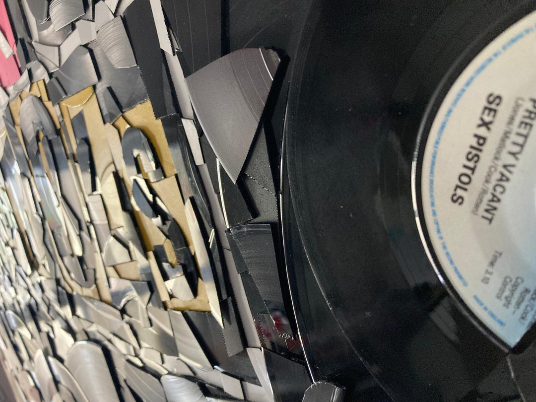 Ed Chapman mosaic artwork featuring the Sex Pistols logo created entirely from destroyed Sex Pistols vinyl records, with fractured black discs and colourful record labels forming a bold punk-inspired composition.