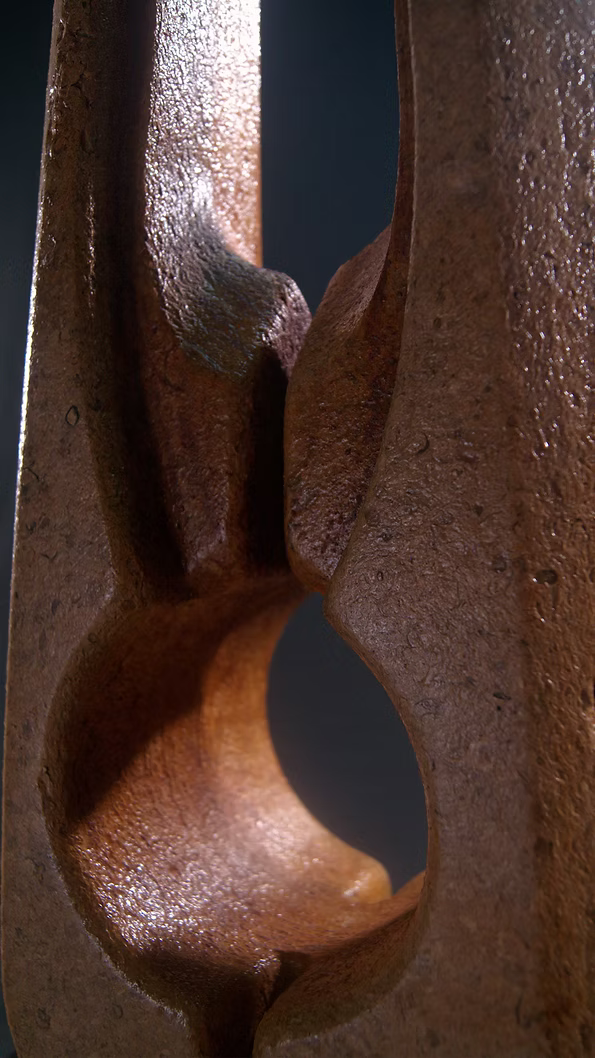 Tall Purbeck stone sculpture with a central vertical opening and tapered peak, standing on a black granite base, showing fossil textures and carved geometry against a dark background.